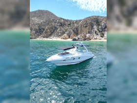 A sleek yacht named 'Coqueto' glides through clear waters, showcasing its elegant design against a stunning coastal backdrop.