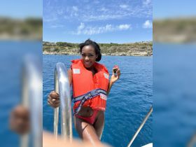A joyful woman in a life jacket poses on a boat, showcasing the vibrant blue ocean — perfect for summer adventures and water activities.