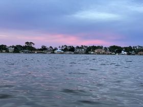 A serene sunset view over the water, showcasing a picturesque coastline with charming homes — perfect for capturing the beauty of waterfront living.