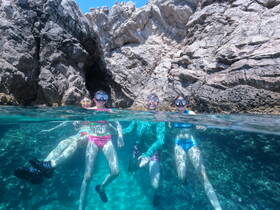 A joyful group of snorkelers enjoys an underwater adventure near stunning rock formations, showcasing the vibrant marine life and clear waters perfect for exploration.