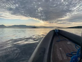 A serene view of the bow of a boat gliding through calm waters, framed by a stunning sky and distant mountains — perfect for showcasing the beauty of boating adventures.