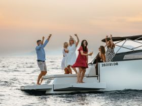 A lively group celebrates on a boat at sunset, enjoying drinks and dancing — the perfect backdrop for unforgettable summer parties on the water.