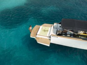 Aerial view of a woman enjoying the clear waters while standing on the platform of a boat, perfect for summer adventures and water activities.