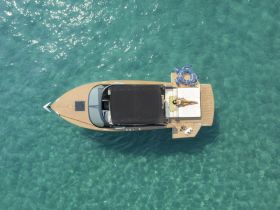 Aerial view of a boat with a person sunbathing on the deck, surrounded by crystal-clear waters — a perfect scene for relaxation and summer fun.