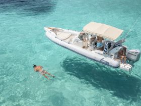 A snorkeler explores the crystal-clear waters while a group enjoys their time aboard a boat, showcasing the perfect blend of adventure and relaxation on the water.