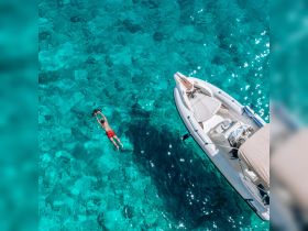 A swimmer enjoys snorkeling in crystal-clear waters beside a sleek boat, showcasing the perfect day for aquatic adventures.