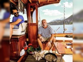 Two men relax inside the cabin of a boat, enjoying the serene views and a casual atmosphere. The interior showcases wooden finishes and fishing gear, perfect for a day on the water.