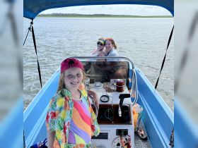 A joyful family enjoys a day on the water, with a child at the helm and two adults smiling in the background — a perfect snapshot of boating fun and adventure.