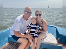 A joyful family enjoys a sunny day on the boat, with a lighthouse in the background — perfect for creating lasting memories on the water.