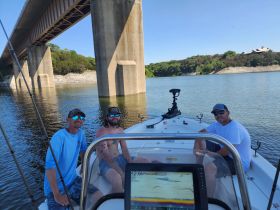 A group of friends enjoys a day on the water, relaxing on their boat under a bridge — perfect for summer outings and fishing adventures.