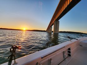 A stunning sunset view from a boat, showcasing a bridge over tranquil waters — perfect for fishing enthusiasts and scenic boat rides.