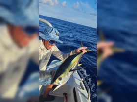 A fisherman proudly holds up his catch aboard a boat in the open ocean, showcasing the thrill of deep-sea fishing adventures.