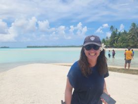 A joyful woman smiles at the beach, surrounded by friends enjoying the clear waters and tropical scenery — a perfect snapshot of island fun.