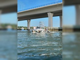 A camouflage speedboat navigates under a bridge, showcasing its unique design while cruising through calm waters.