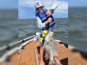 A young angler proudly displays his catch while fishing on a boat, showcasing the joy of fishing adventures for kids.