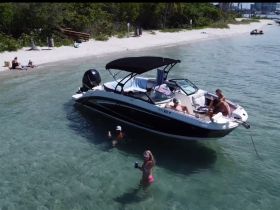 A lively group enjoys a beach day with a pontoon boat, swimming in clear waters and soaking up the sun — the perfect setting for a fun day on the water.