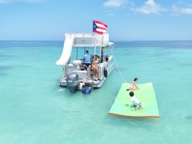 Children enjoy a fun day on a floating mat next to a boat in crystal-clear waters, showcasing the perfect family-friendly adventure on the water.