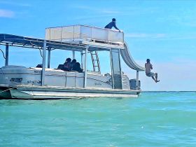 A thrilling moment as a young boy prepares to jump from a water slide on a pontoon boat, while others enjoy the sun and sea — perfect for family fun on the water.
