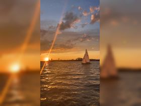 A serene sunset view featuring a sailboat gliding across the water with a stunning city skyline in the background, perfect for capturing the beauty of evening sailing adventures.
