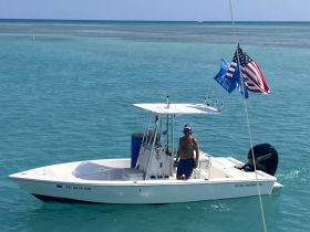 A man stands aboard a Cobia boat in the clear blue ocean, showcasing a perfect day for fishing or leisure on the water.