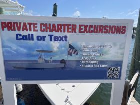A sign advertising private charter excursions, featuring various activities such as snorkeling and sunset cruises, with contact information for bookings.