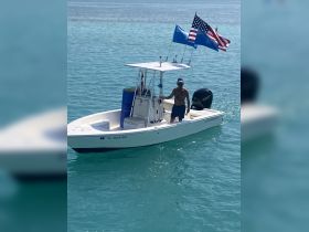 A man navigates a boat adorned with flags in clear turquoise waters, showcasing a vibrant day on the water.
