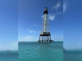 A stunning view of a lighthouse standing tall in the turquoise waters, with boats nearby, perfect for capturing the essence of a boating adventure.