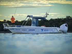 A fisherman casts his line from the deck of the Dreamcatcher boat during a serene sunset, showcasing the perfect fishing experience on the water.