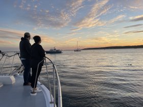 A couple enjoys a stunning sunset view from the bow of a boat, creating a perfect romantic atmosphere on the water.