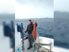 A fisherman proudly displays his catch of a large squid while out on the ocean, showcasing the thrill of fishing adventures.