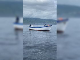 A fishing boat navigates the calm waters, showcasing its structure against a scenic backdrop of hills and cloudy skies.