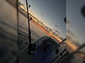 A serene sunset view from the deck of a speedboat, showcasing fishing gear and calm waters — perfect for evening fishing trips.