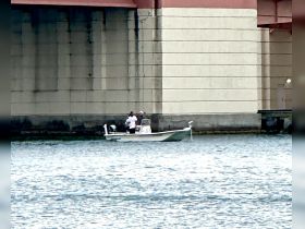 A small boat with two people fishing beneath a bridge, showcasing a serene moment on the water.