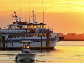 A scenic sunset view of a small boat approaching the dock, with a larger fishing vessel in the background, creating a picturesque marina atmosphere.
