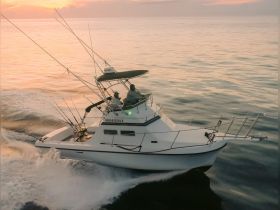 A fishing boat navigates through calm waters at sunset, showcasing an exciting fishing adventure on the open sea.