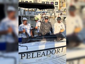 A group of anglers proudly displays their catch of the day, a marlin, aboard the boat 'Peleador I' in Cabo San Lucas — a memorable fishing experience on the water.