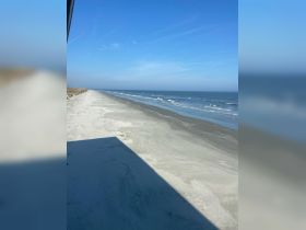 A view of a beach and ocean under a clear blue sky, with an unclear angle and shadow in the foreground.