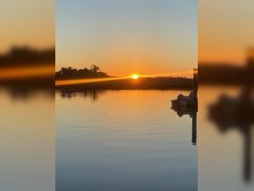 A serene sunset over calm waters, with a glimpse of a docked boat, creating a picturesque scene perfect for evening reflections.