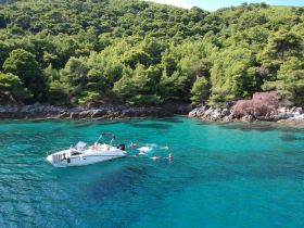 A group enjoys a refreshing swim in the crystal-clear waters near a scenic coastline, with a boat anchored nearby — perfect for summer adventures and beach outings.