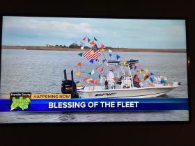 A festive scene from the 'Blessing of the Fleet' event, showcasing a decorated boat with a group of people celebrating on the water.
