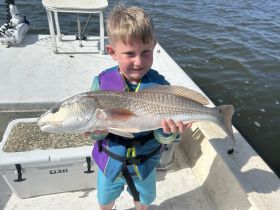 A young boy proudly holds up a freshly caught redfish while on a boat, showcasing a memorable fishing experience on the water.