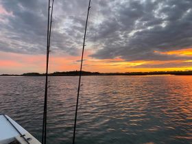 A stunning sunset view over calm waters, with fishing rods in the foreground, creating a perfect backdrop for a peaceful evening on the water.