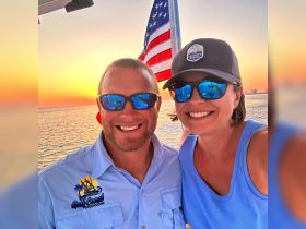 A couple smiles for a selfie against a stunning sunset backdrop on the water, capturing a perfect moment of joy and celebration during their boating adventure.