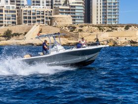 A speedboat cuts through the waves with two passengers enjoying the ride, showcasing the thrill of boating adventures against a scenic backdrop.