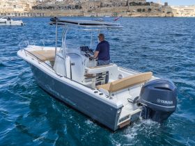 A person navigates a White Shark boat powered by a Yamaha engine, cruising through clear waters with a scenic backdrop of coastal architecture.