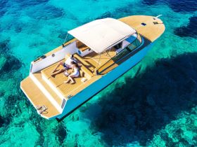 A couple relaxes on the deck of a stylish boat, soaking up the sun against a backdrop of stunning turquoise waters — an ideal scene for a romantic getaway or a day of leisure on the water.