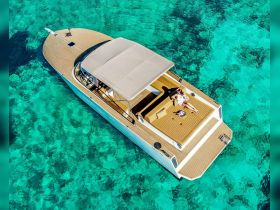 Aerial view of a woman relaxing on the deck of a stylish yacht, surrounded by crystal-clear turquoise waters — an ideal setting for sunbathing and enjoying the ocean.