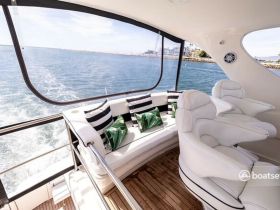 A stylish interior view of a yacht's seating area, featuring comfortable white chairs and decorative cushions, perfect for relaxing while enjoying the scenic ocean views.