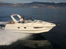 A couple enjoys a thrilling ride on a sleek yacht, cruising through serene waters with stunning coastal views in the background.