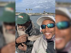 Two friends share a moment on a fishing trip, showcasing smiles and camaraderie on the water.
